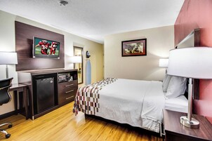 Una habitación de hotel con una cama, un escritorio, un televisor y un cuadro en la pared.