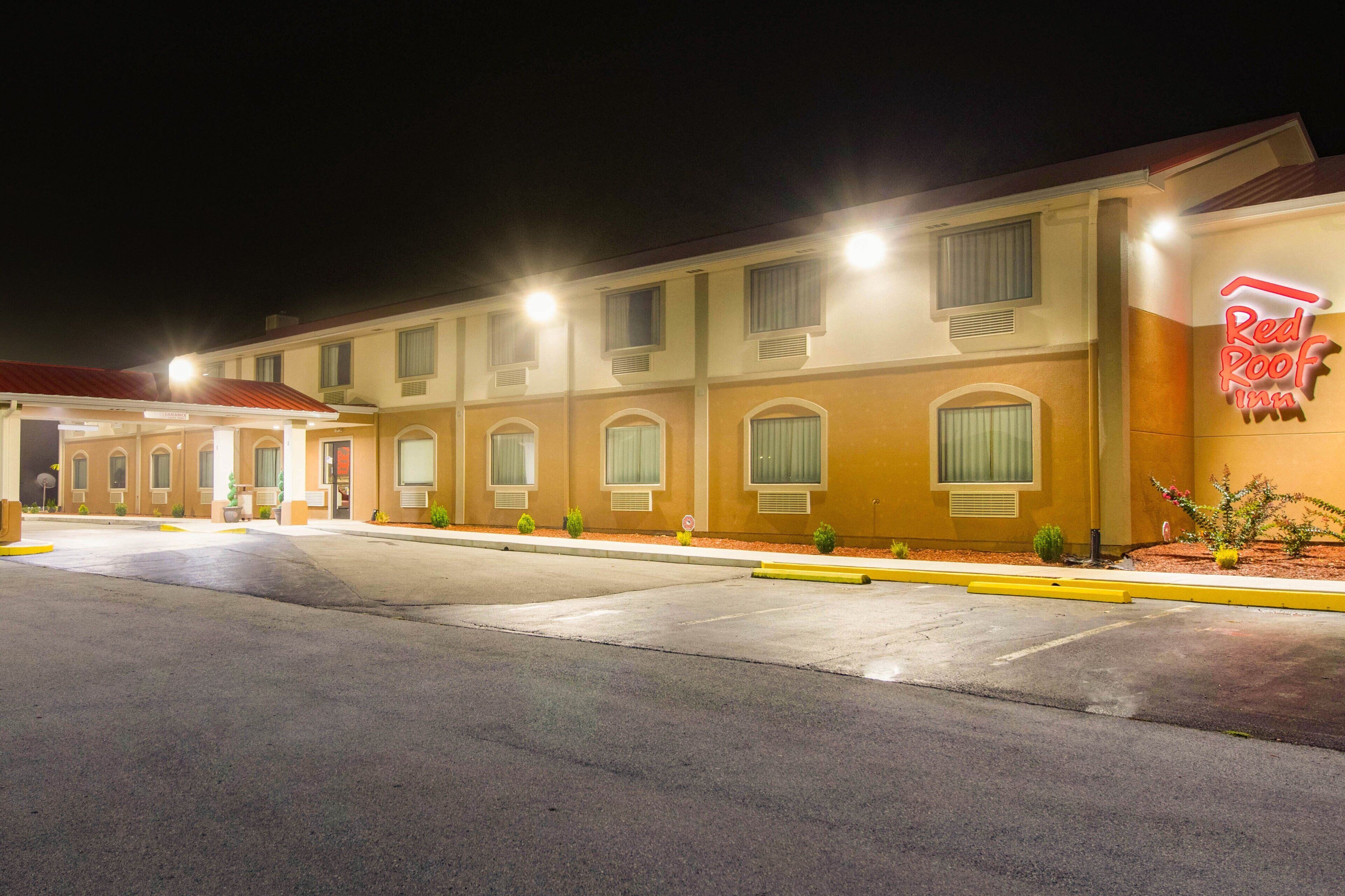 A Red Roof Inn with a parking lot and a building facade featuring multiple windows and a neon sign.