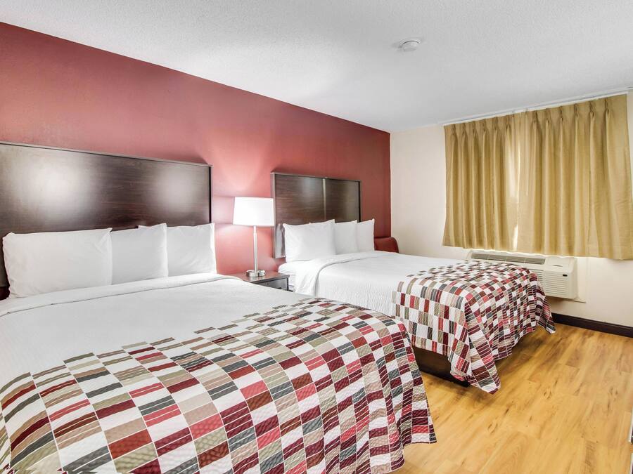 Habitación de hotel con dos camas, una mesita de noche con lámpara, ventana con cortinas y luz en el techo.