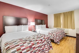 Habitación de hotel con dos camas, una mesita de noche con lámpara, ventana con cortinas y luz en el techo.
