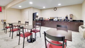 A dining area with tables and chairs, a kitchen with appliances, and a clock on the wall. - Red Roof Inn Franklin, KY (Franklin)