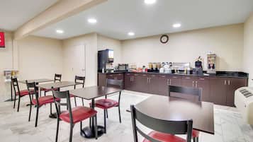 A dining area with tables and chairs, a kitchen with appliances, and a clock on the wall.