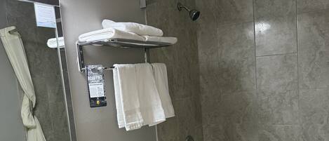 A modern bathroom with a sink, toilet, and bathtub. There is a towel rack with towels, a mirror, and a shower curtain.
