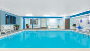 A swimming pool with blue and white tiled walls, a blue door, and a blue chair near the pool.