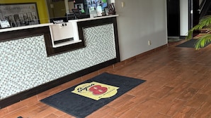 A hotel reception area with a tiled wall, a reception desk, and a digital screen displaying images.