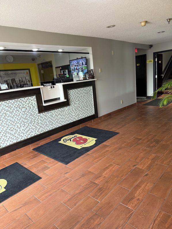 A hotel reception area with a tiled wall, a reception desk, and a digital screen displaying images.