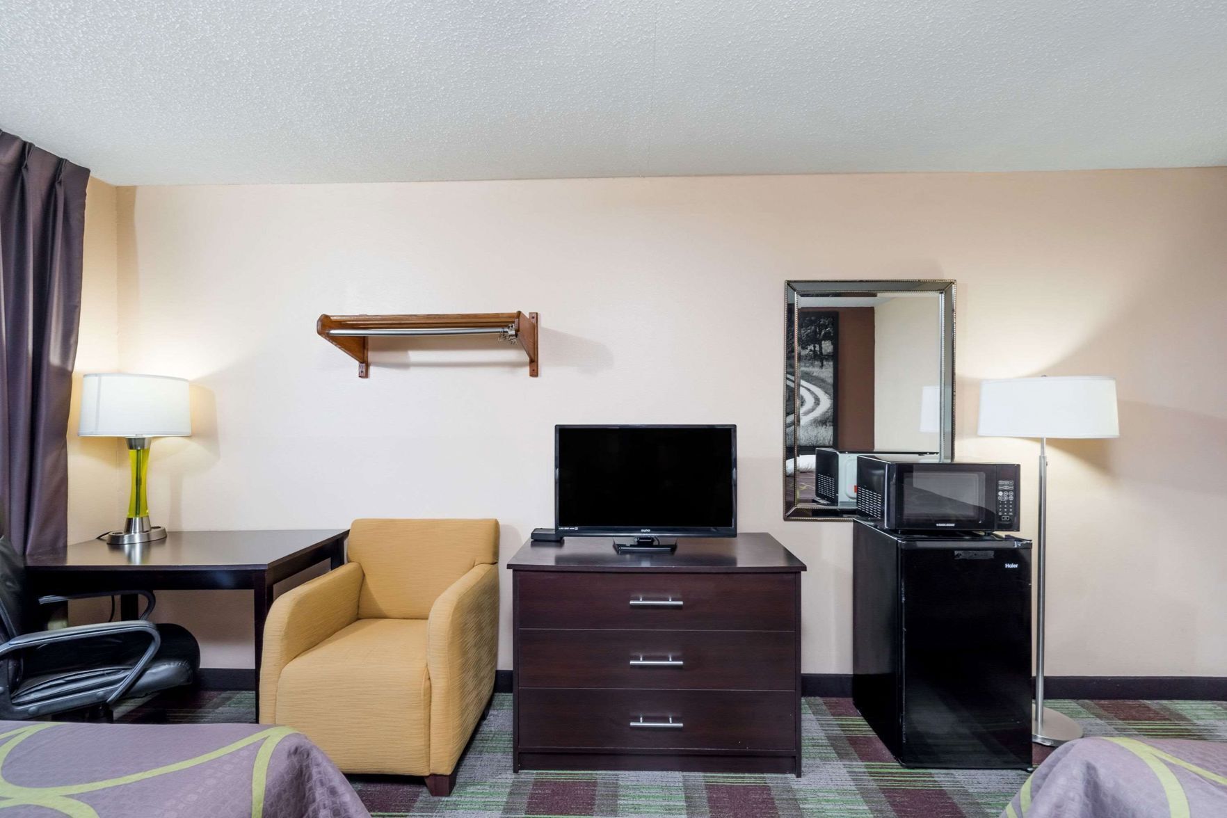 Ein Hotelzimmer mit Bett, Schreibtisch mit Stuhl, Fernseher, Kommode, Mikrowelle und Spiegel.