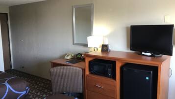 A hotel room with a wooden desk, a television, a microwave, a refrigerator, a chair, and a bed with patterned bedding.