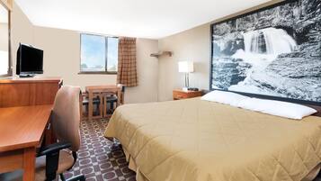 A hotel room with a bed, a desk with a chair, a television, a window with curtains, and a large wall-mounted picture of a waterfall.