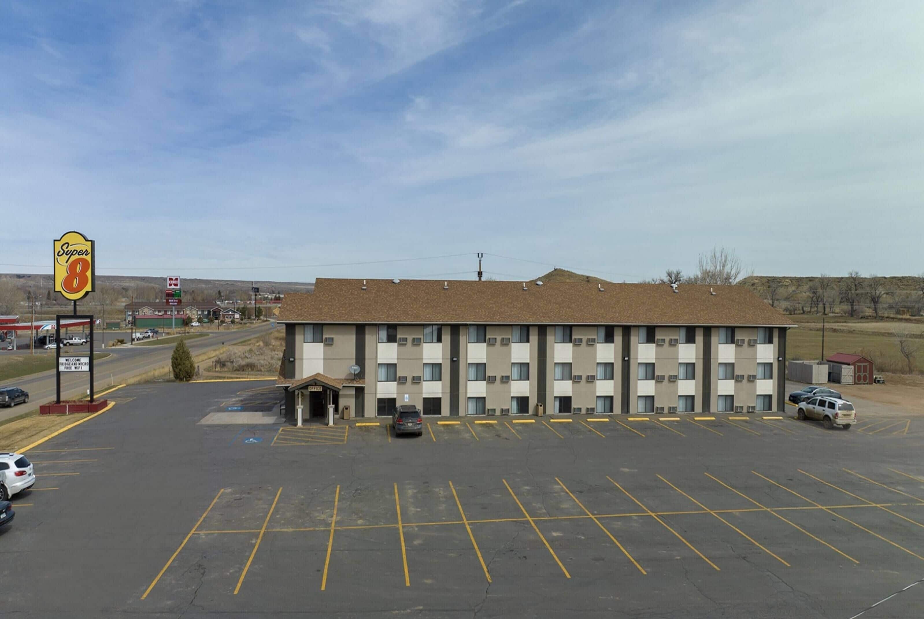 A Super 8 motel with a parking lot, a road in the background, and a clear sky.