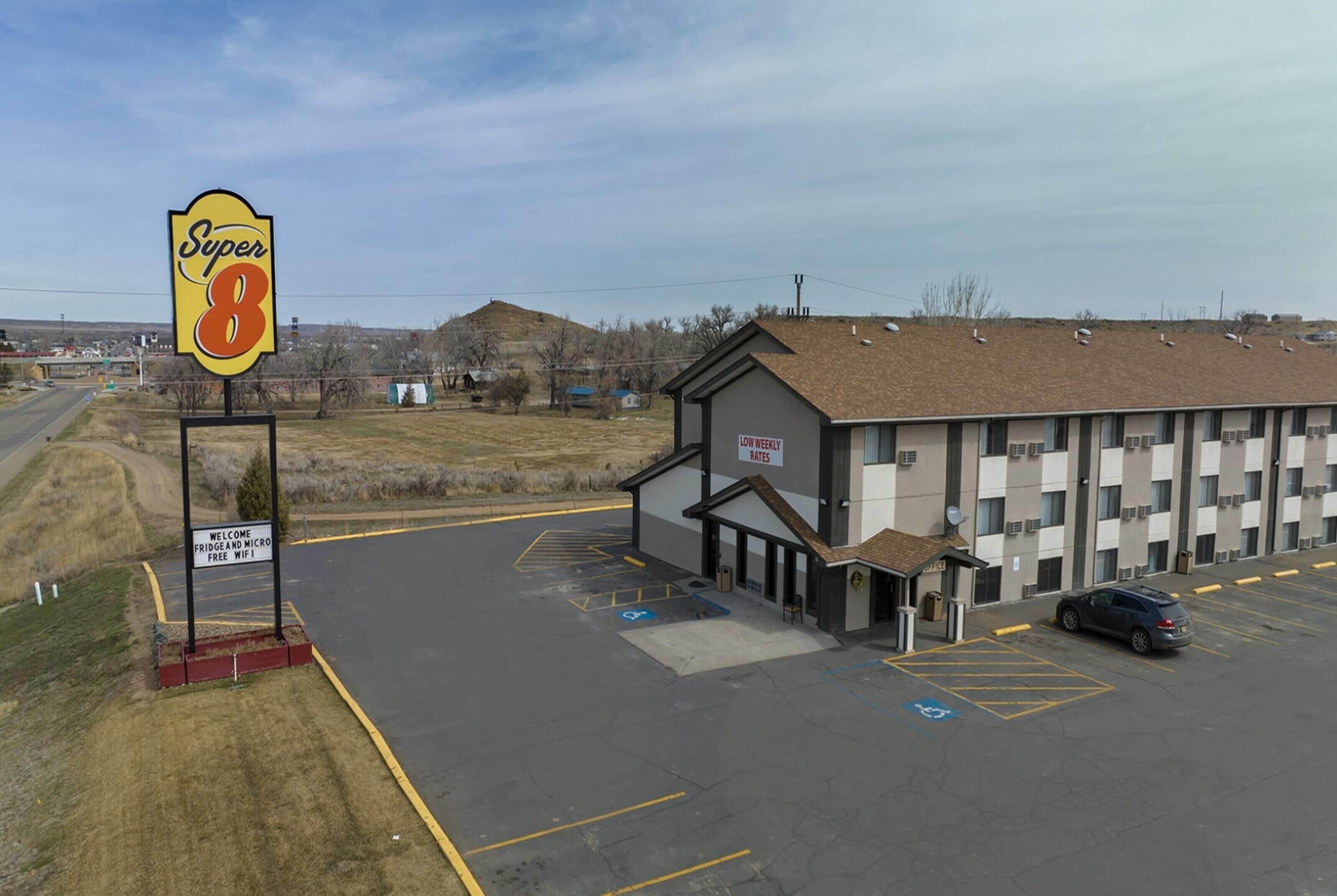A Super 8 motel with a signboard, parking lot, and a building with a sign indicating low weekly rates.