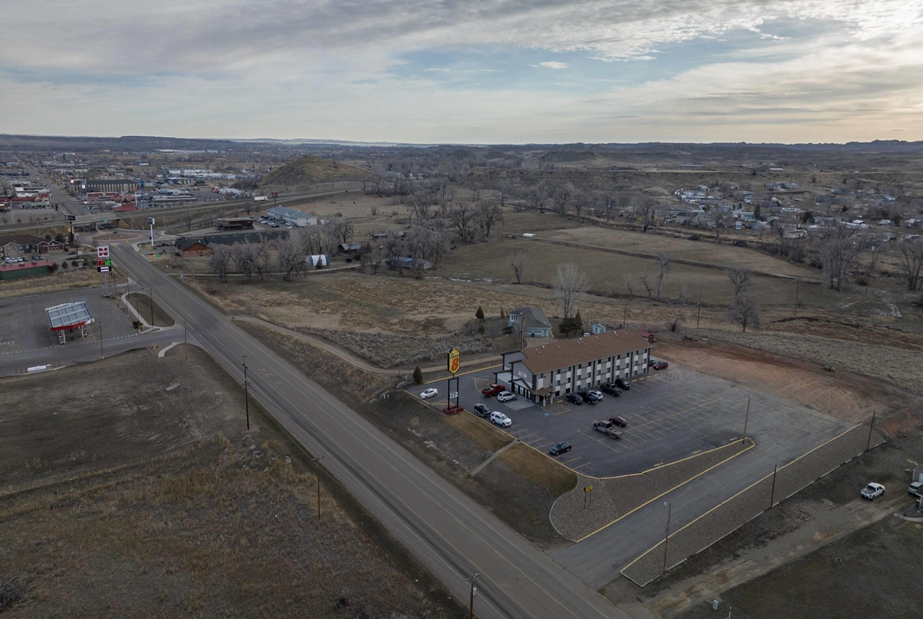 An aerial view of a gas station with a parking lot, surrounded by open fields and sparse buildings.