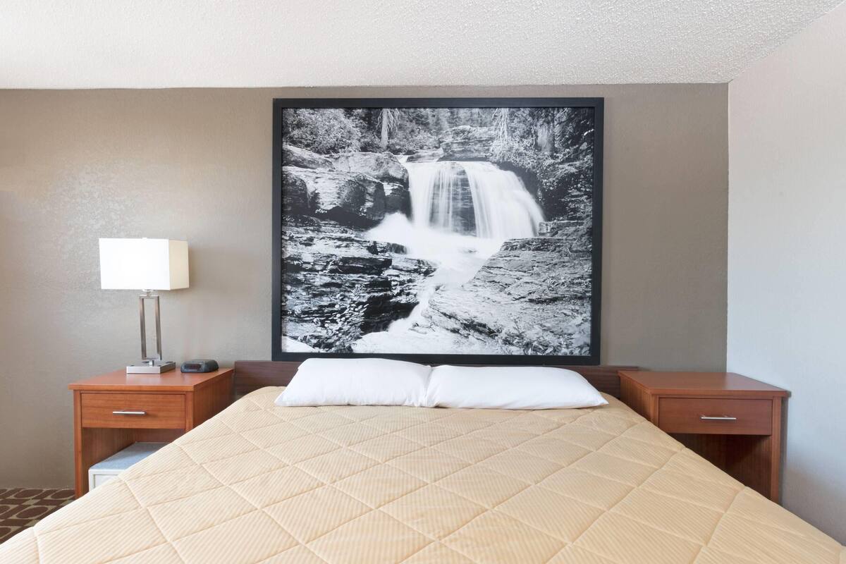 Ett hotellrum med en säng, ett nattduksbord med en lampa och ett stort inramat fotografi av ett vattenfall på väggen.