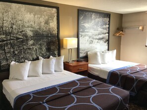 A hotel room with two beds, each with white linens and brown patterned bedspreads. There are two large framed pictures on the wall, one depicting a forest scene and the other a waterfall. A bedside table with a lamp and a small clock is visible. - Super 8 by Wyndham Miles City (Miles City)