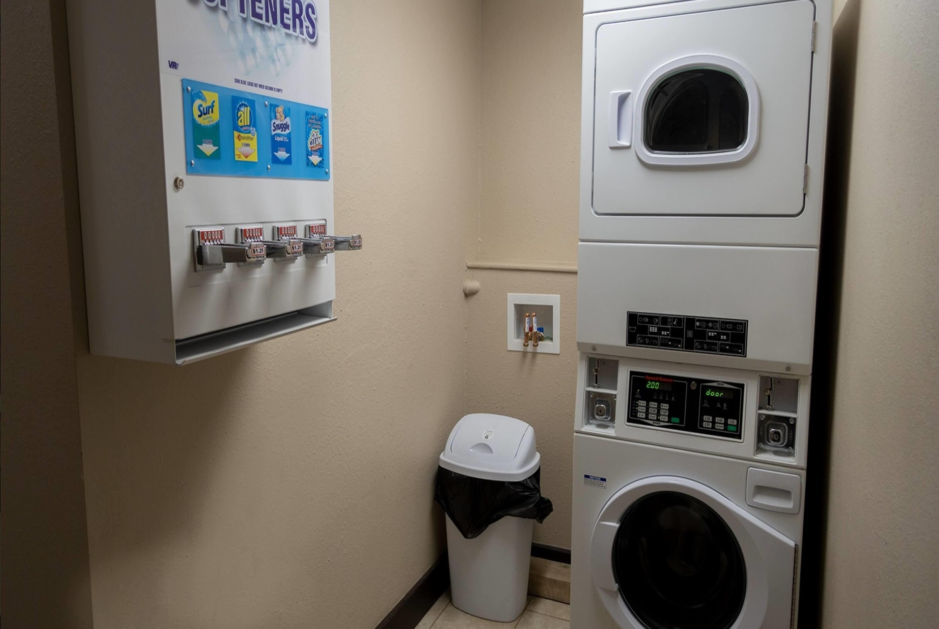 Un cuarto de lavandería con lavadora, secadora y un cubo de basura.
