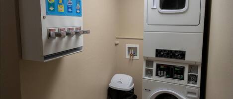 Un cuarto de lavandería con lavadora, secadora y un cubo de basura.