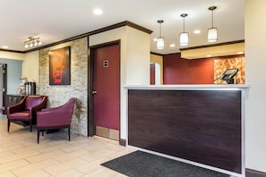A reception area with a stone wall, a red door, a reception desk, and two leather chairs.
