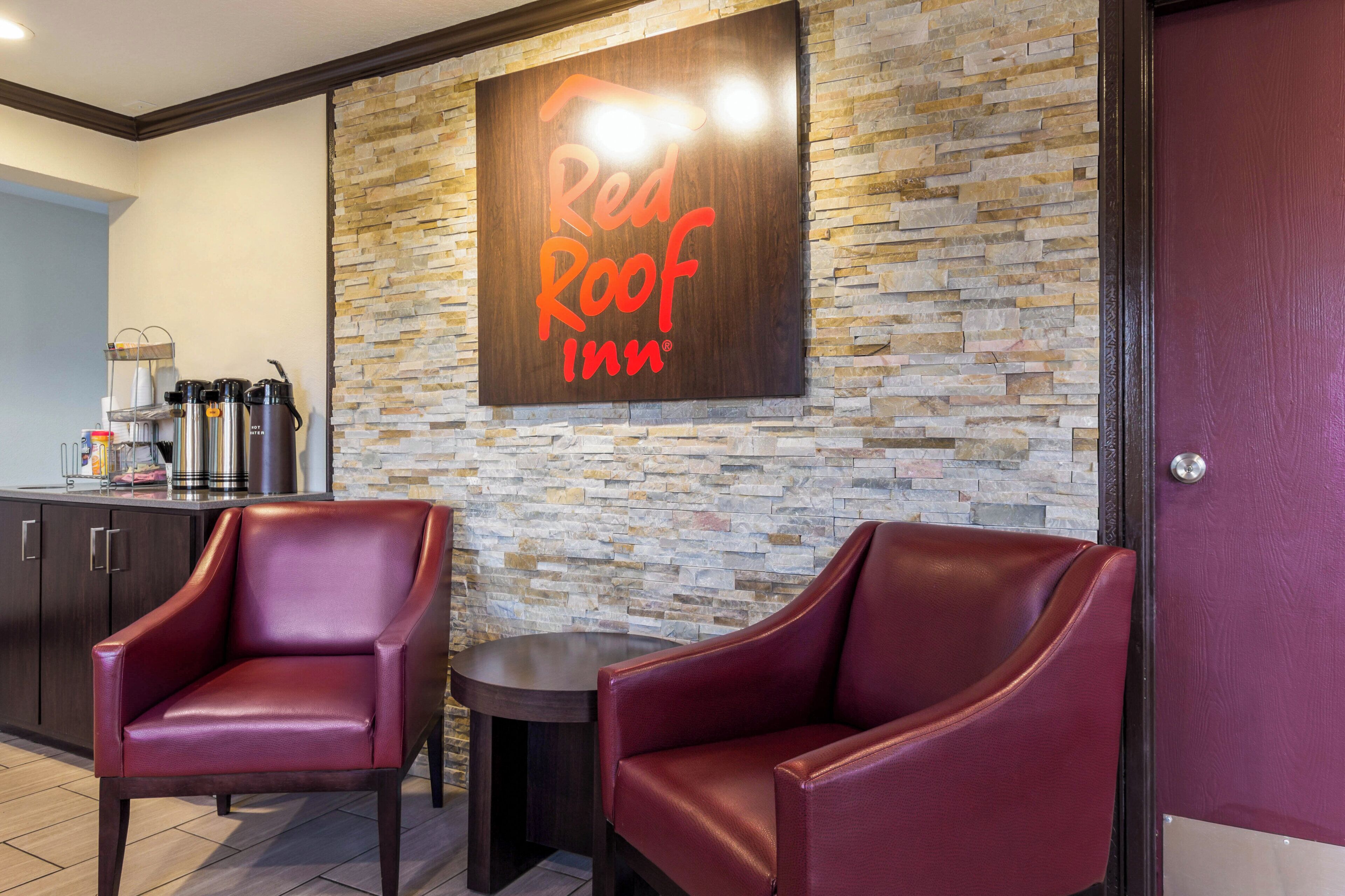 Red Roof Inn -hotellin aula, jossa on kiviseinät, nahkaverhoillut nojatuolit ja kahvinautintoalue.