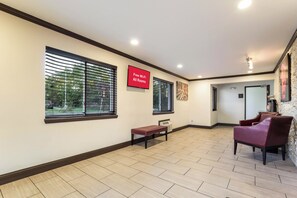 A hotel lobby with a flat-screen TV displaying 'Free Wi-Fi All Rooms,' a bench, a fireplace, and a seating area with chairs.