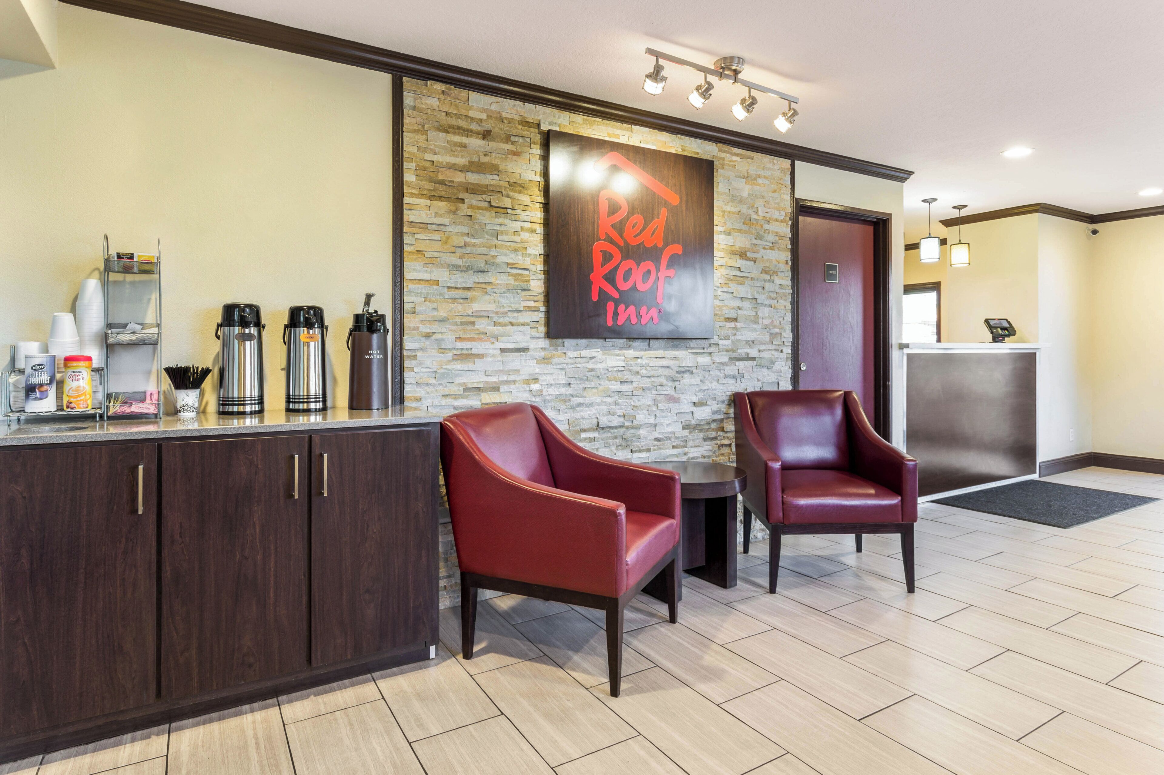 Ein Empfangsbereich eines Red Roof Inn mit Steinwand, einer Kaffeestation und Ledersesseln.