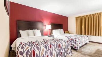 A hotel room with two beds, a red accent wall, a wooden floor, and a window with curtains.