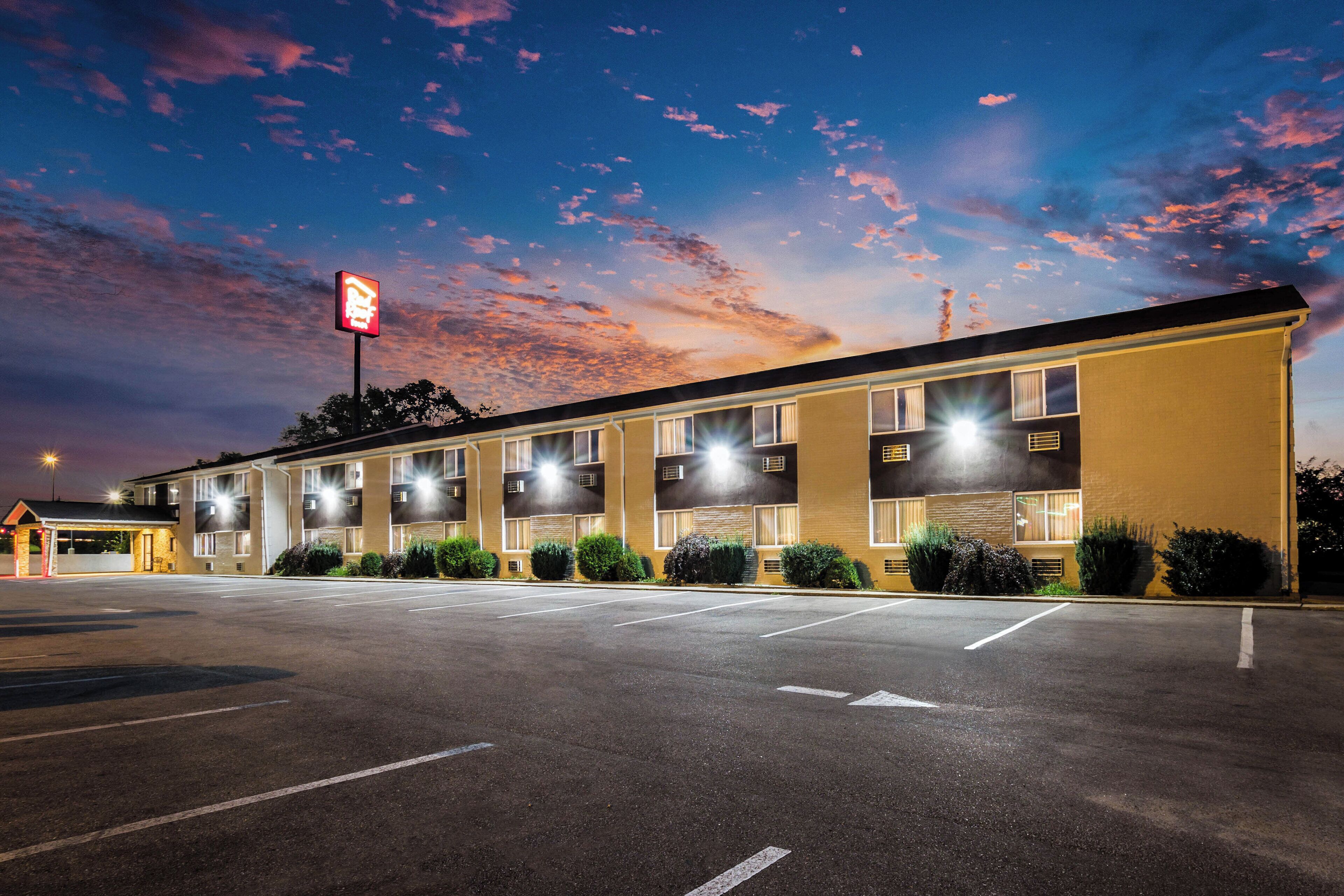 A motel with a row of rooms, a parking lot, and a clear sky with clouds.