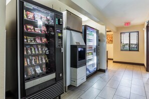 A row of vending machines in a hallway with a tiled floor and a door with an exit sign. - Red Roof Inn Dry Ridge (Dry Ridge)