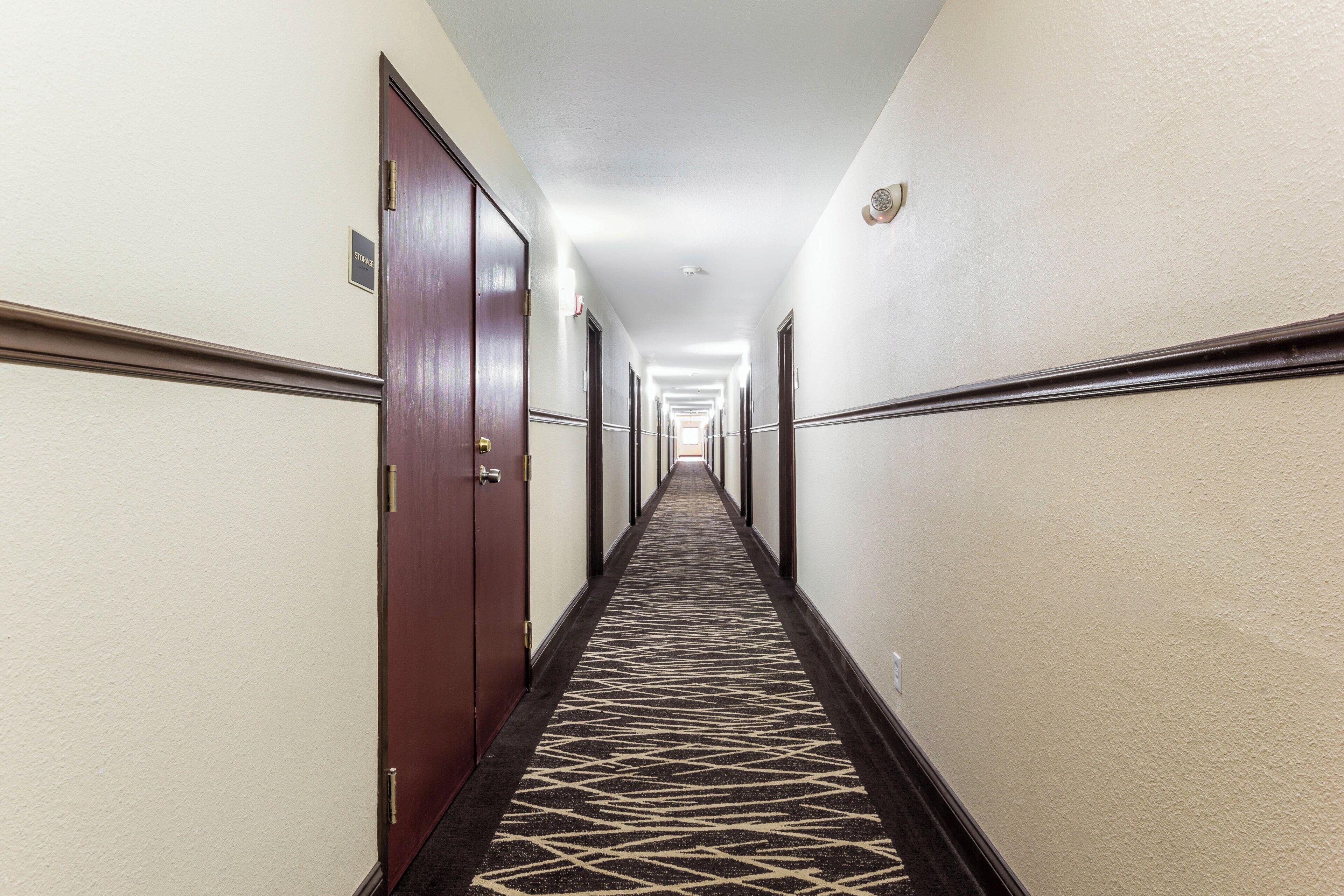 A hotel hallway with doors on both sides, a patterned carpet, and a sign indicating storage.