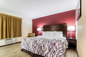 Una habitación de hotel con cama, dos lámparas de noche, una silla, una mesita de noche y aire acondicionado de pared.