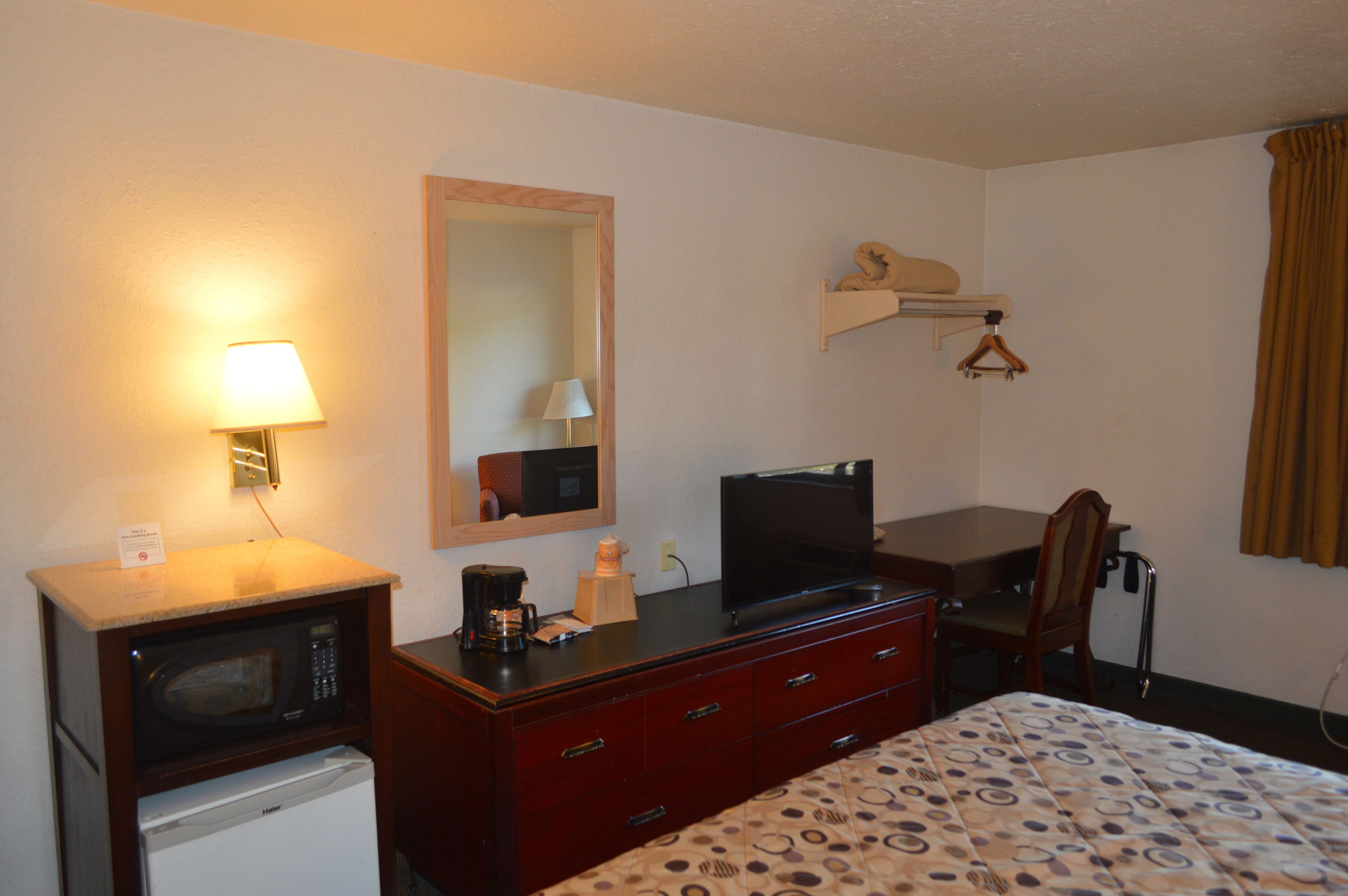 Hotelkamer met een bed, een bureau met een computer, een magnetron, een koffiezetapparaat, een spiegel en een plank met een kapstok.