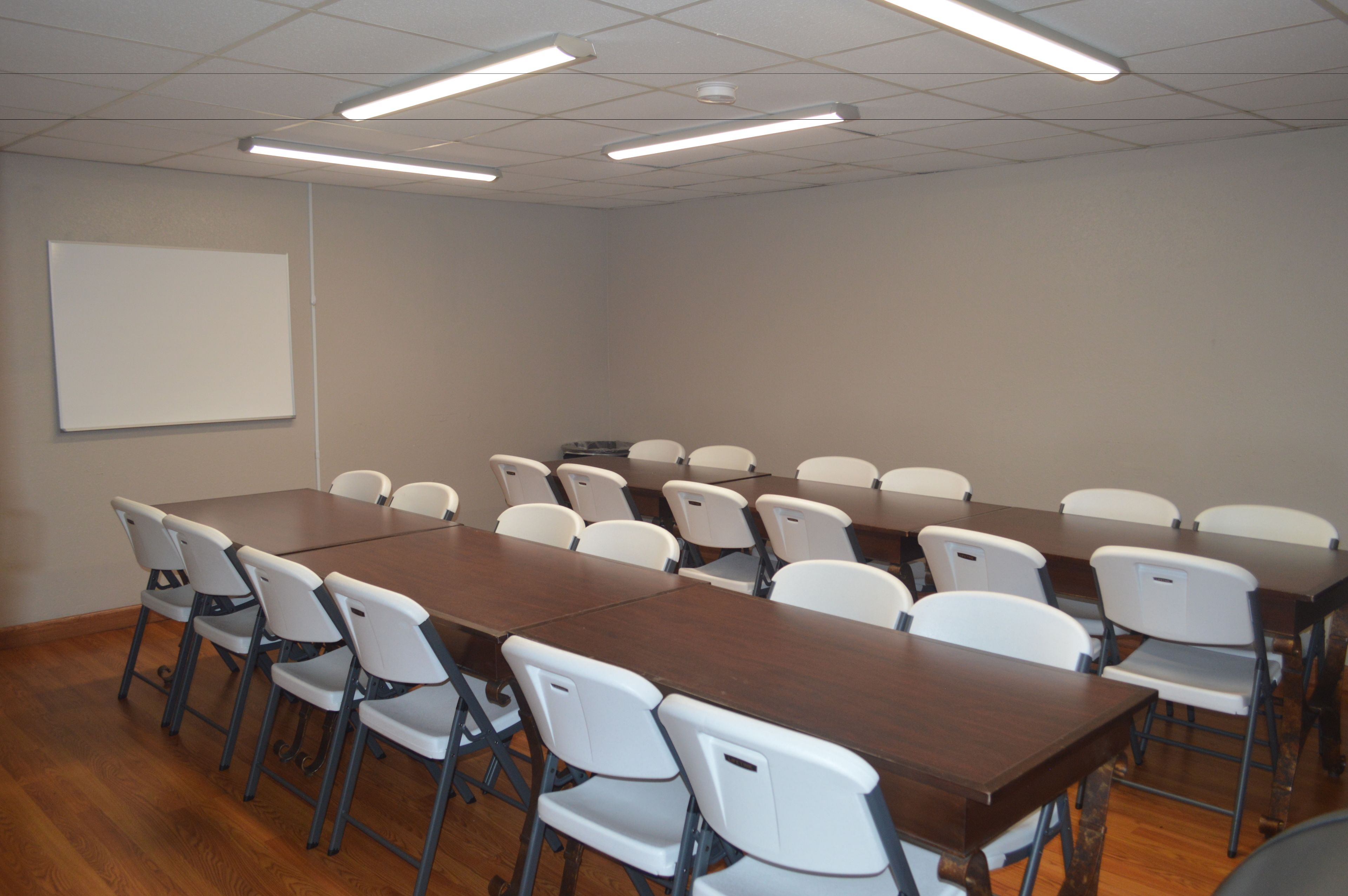 A conference room with a long table, white chairs, and a whiteboard on the wall.