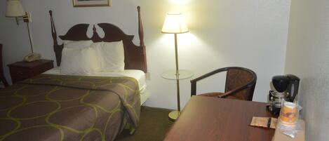 Ein Hotelzimmer mit Bett, Nachttisch, Lampe, Sessel und Tisch mit Kaffeemaschine und Getränkebehälter.