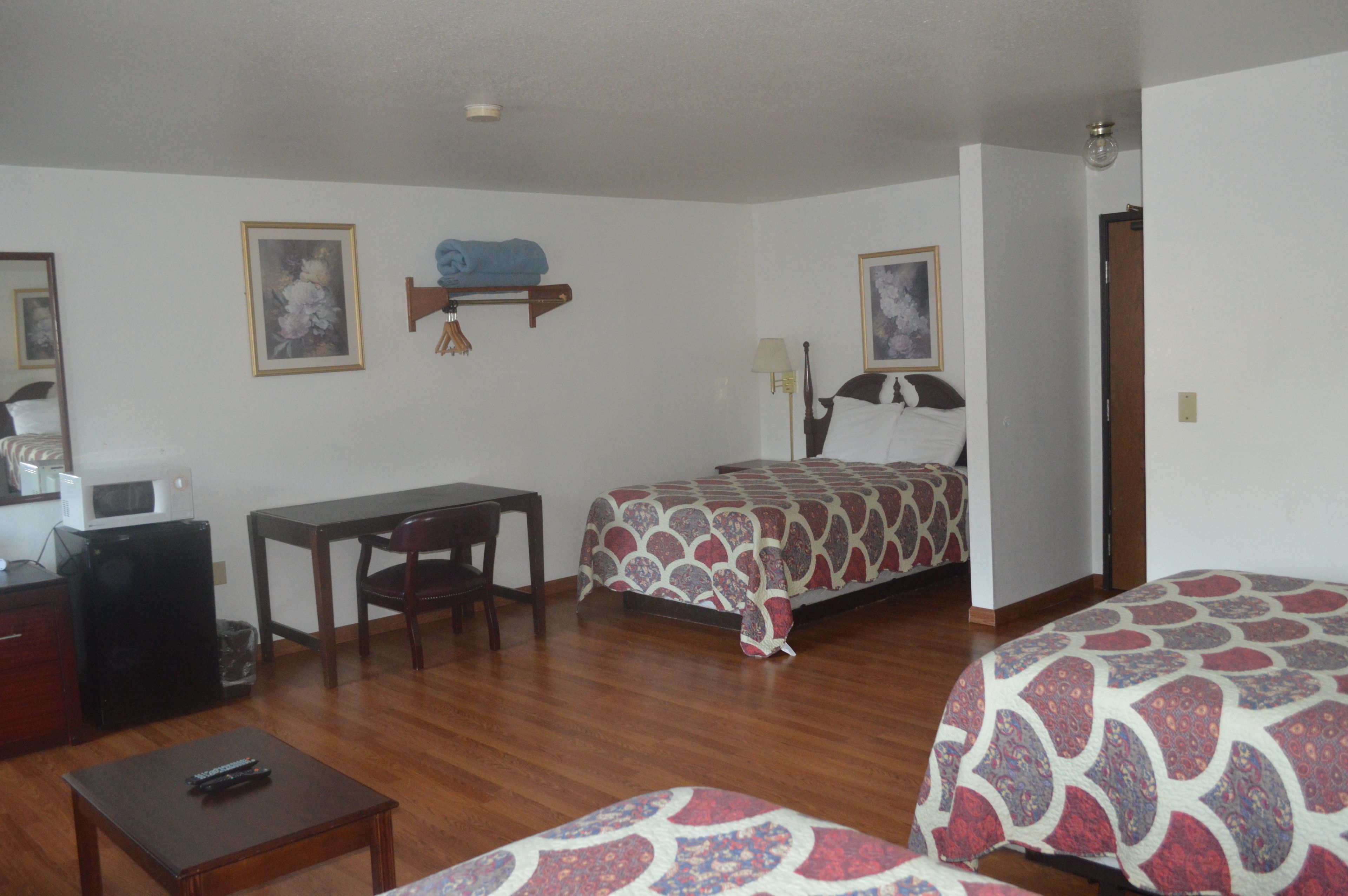 A hotel room with a bed, a desk, a chair, a small table, and a microwave.