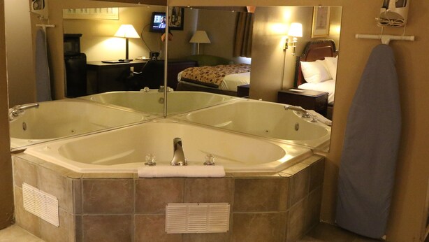 A bathroom with a large freestanding bathtub, a mirror, a towel rack, and a television in the background. - American Elite Inn (Hazard)
