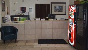 A reception area with a counter, a refrigerator, a vending machine, and a chair. - American Elite Inn (Hazard)