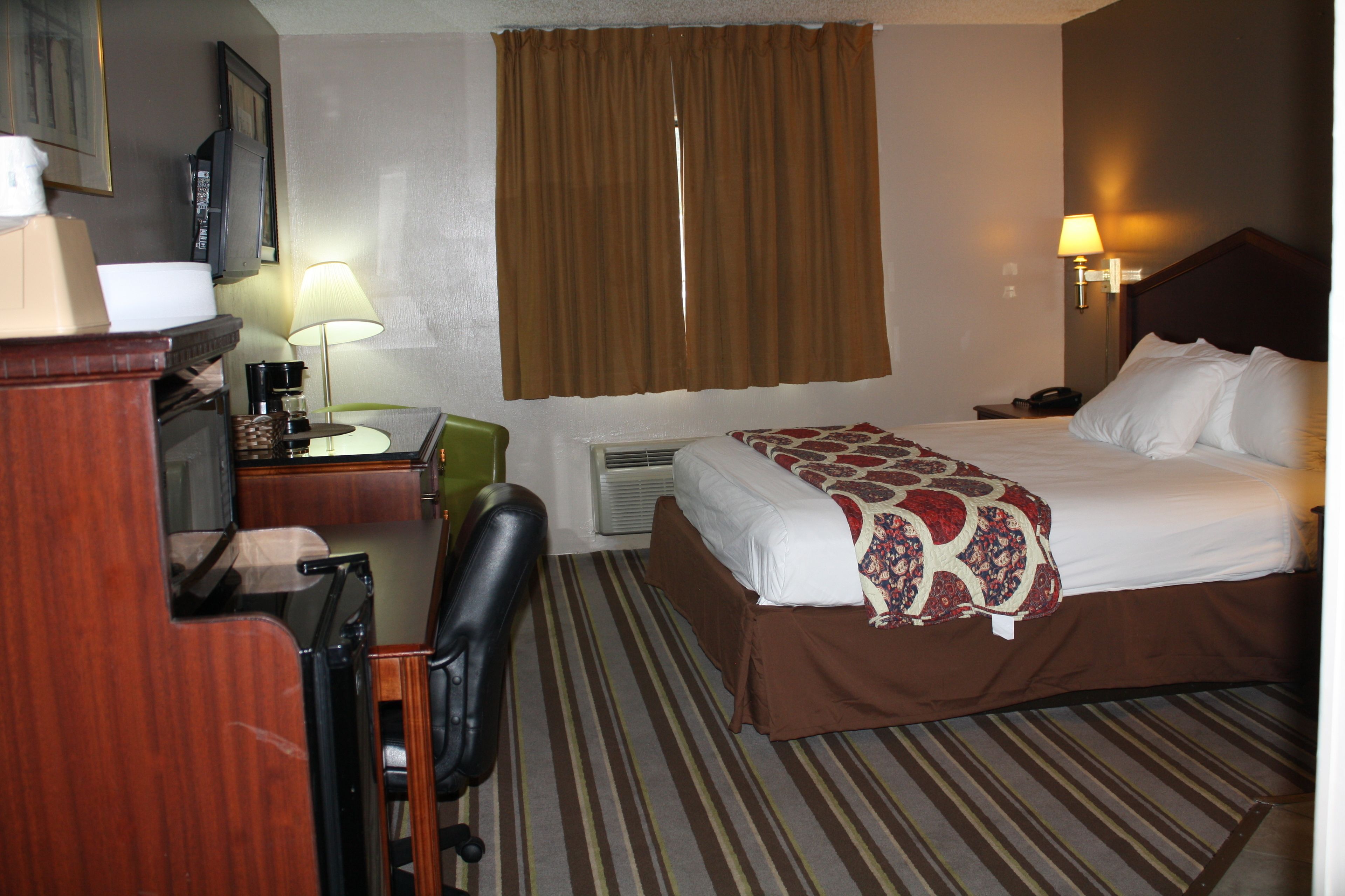 Una habitación de hotel con cama, escritorio, silla, televisor y lámpara.