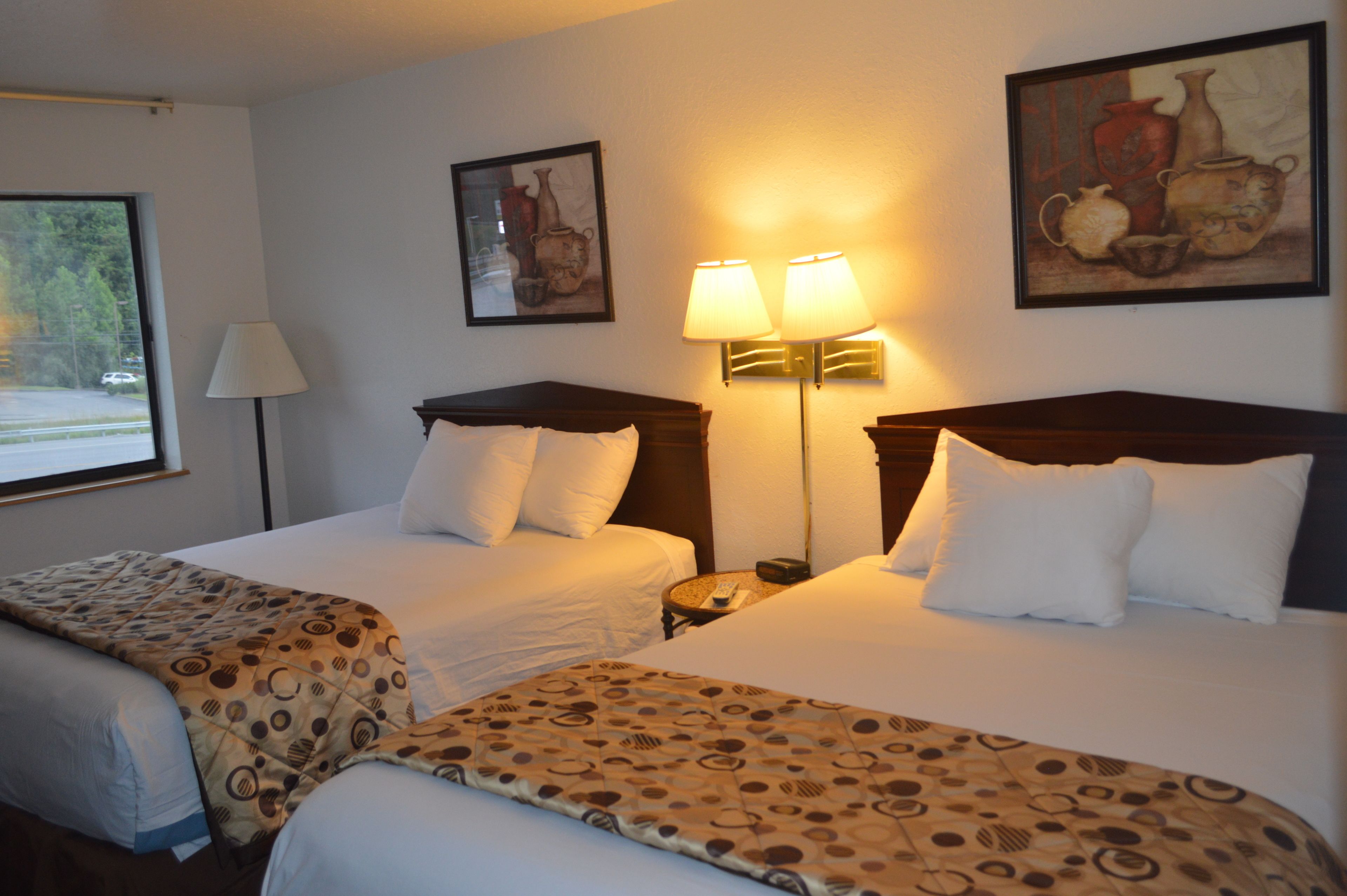 A hotel room with two beds, a nightstand, a lamp, and a painting on the wall.