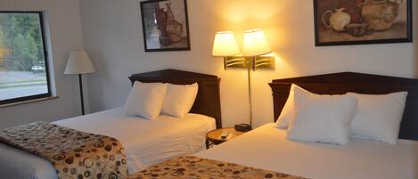 A hotel room with two beds, a nightstand, a lamp, and a painting on the wall.