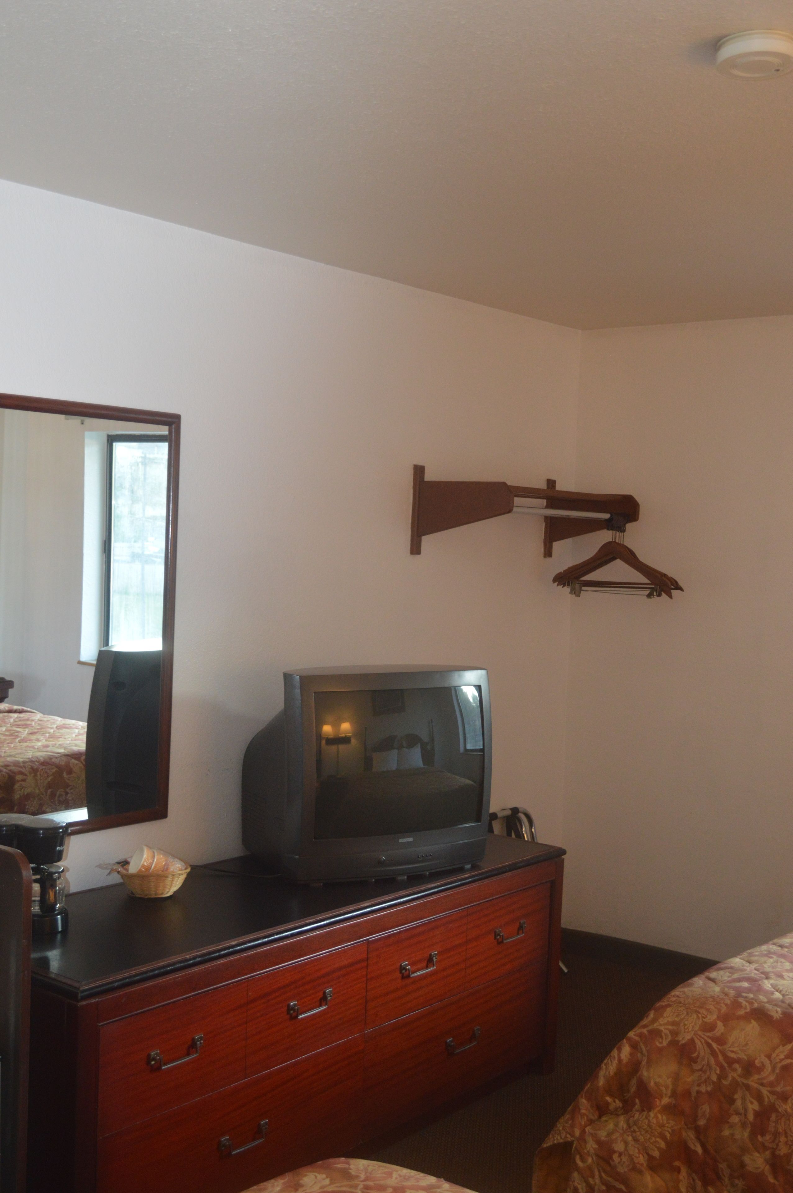 Een hotelkamer met een houten dressoir, een televisie erboven, een spiegel en een wandhouder voor kleding.