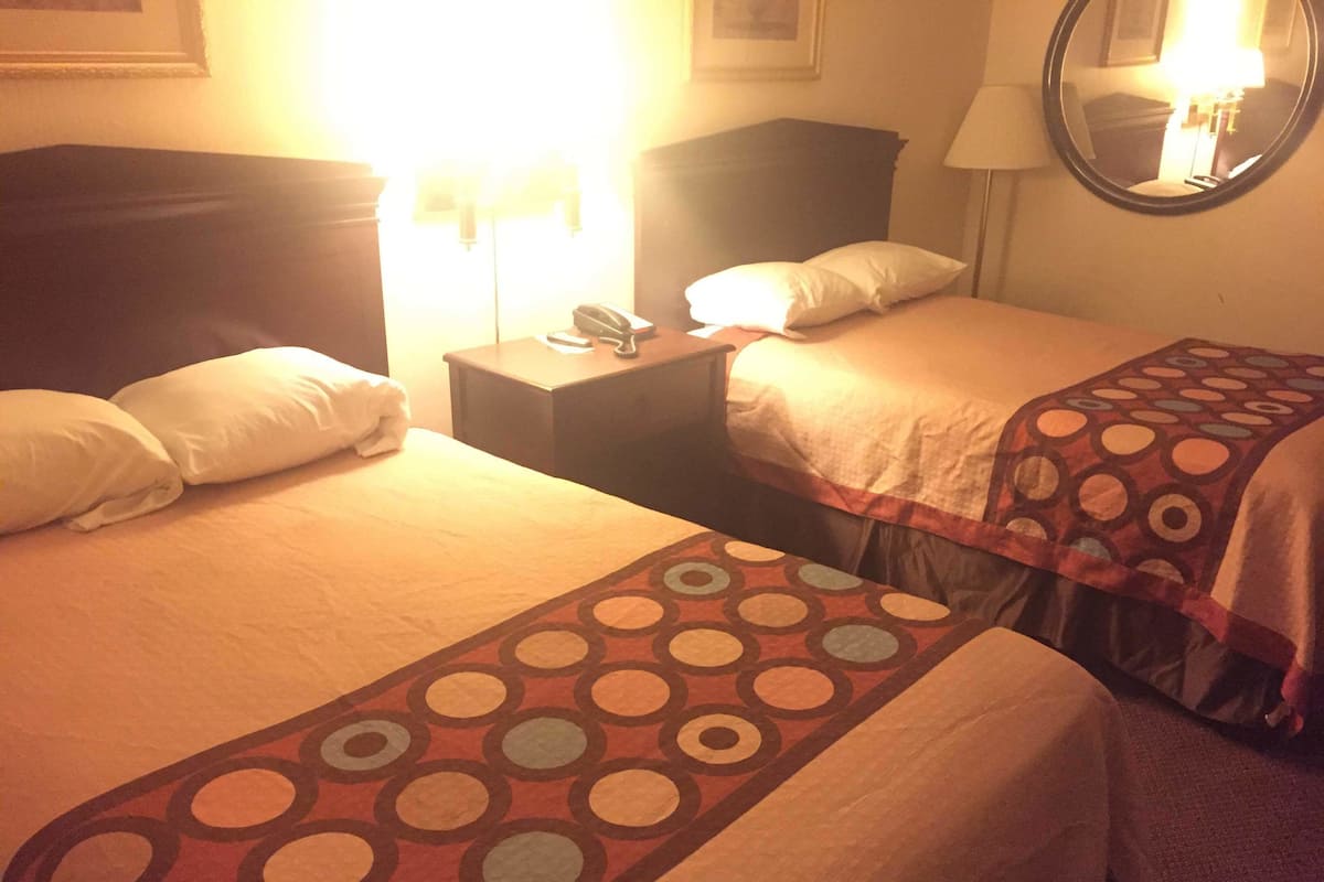 A hotel room with two beds, a bedside table with a lamp, and a mirror on the wall.