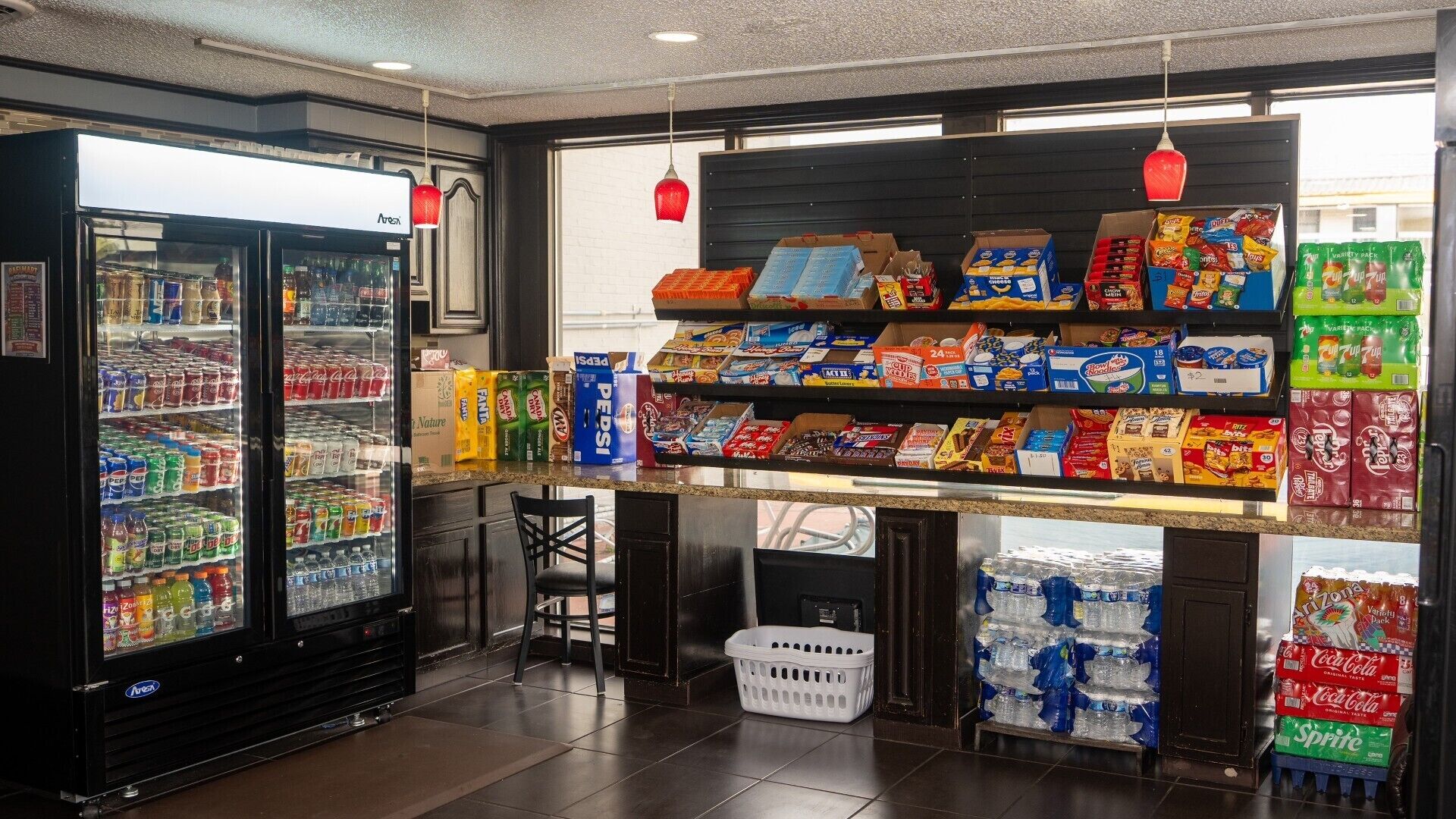 A convenience store with a refrigerated beverage cooler, shelves stocked with snacks, and a variety of packaged goods.