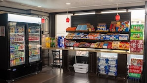 Una tienda de conveniencia con un refrigerador para bebidas, estantes llenos de botanas y una variedad de productos envasados.