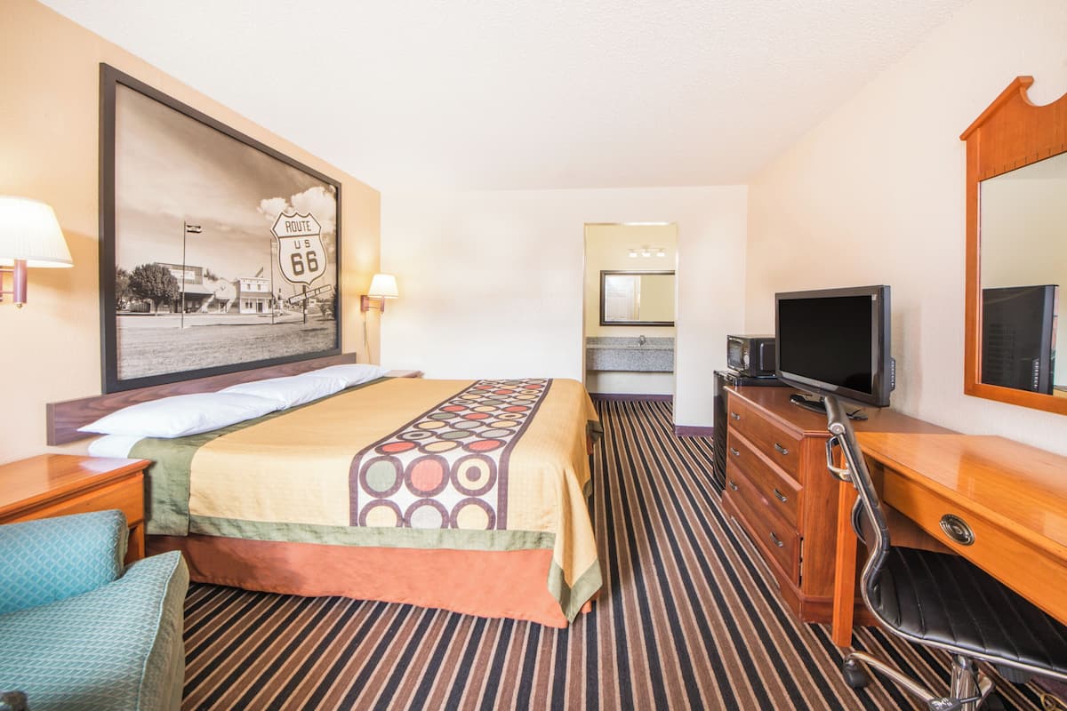 Una habitación de hotel con cama, televisión, cómoda, espejo y un cuadro en la pared.