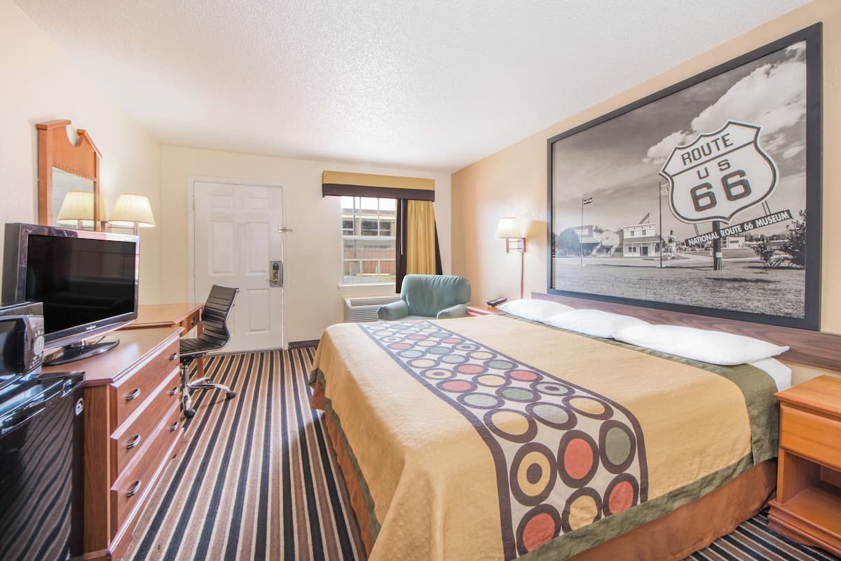 Habitación de hotel con una cama, un escritorio con una computadora, un televisor y un cartel grande de la Ruta 66.