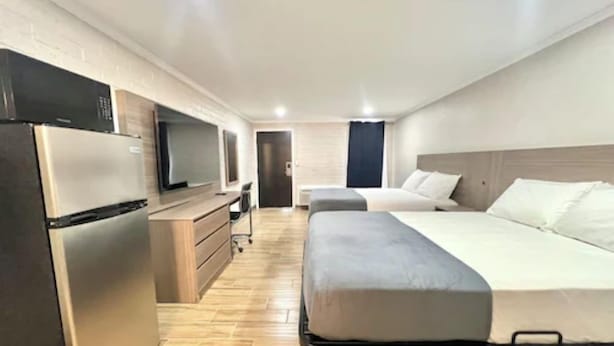 A modern hotel room with a bed, a desk, a television, and a refrigerator.