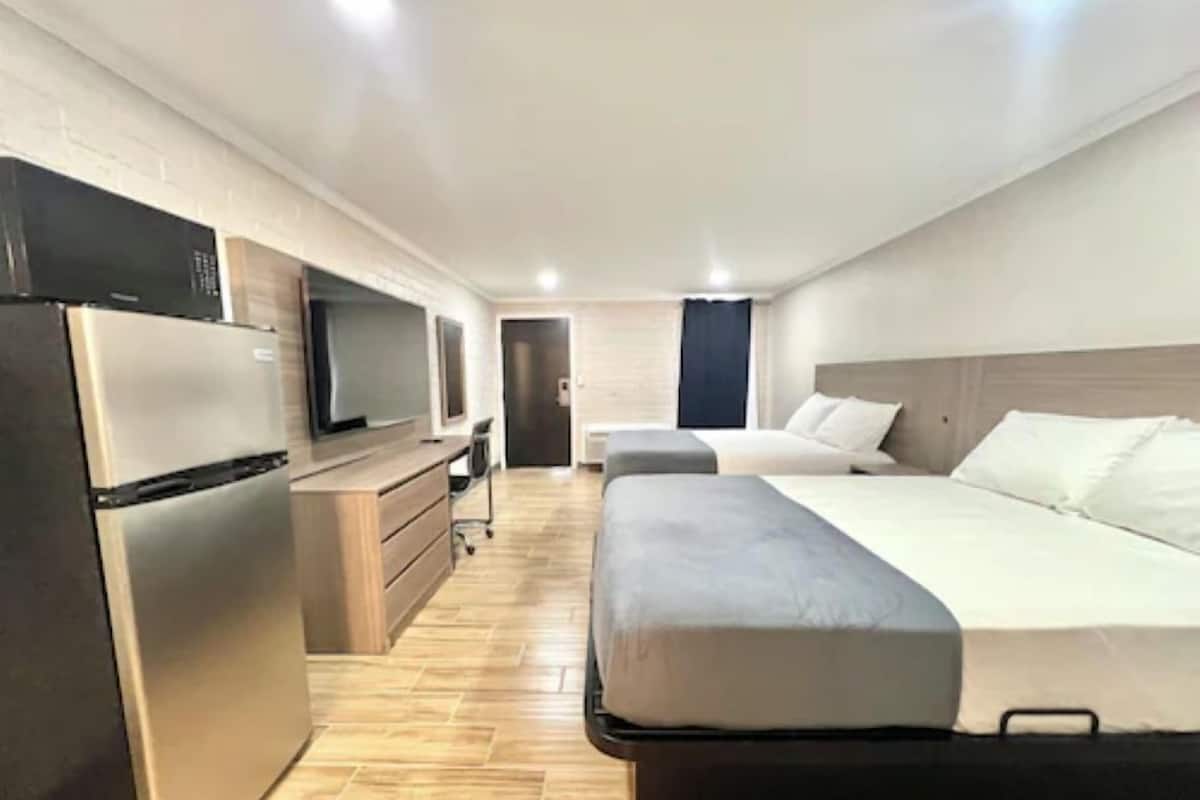 Una habitación de hotel con cama, escritorio, televisor y refrigerador.