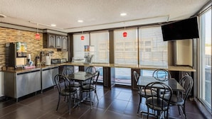 A restaurant with a kitchen counter, dining tables, chairs, and a TV mounted on the wall.