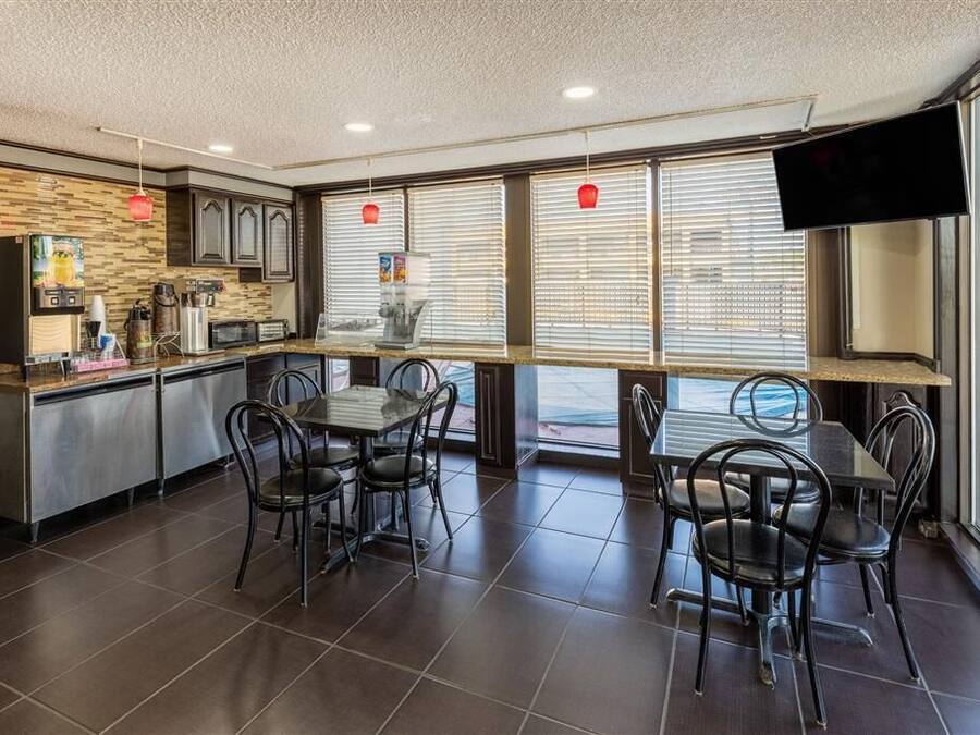 A restaurant with a kitchen counter, dining tables, chairs, and a TV mounted on the wall.