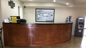 A reception desk with a framed welcome sign, a yellow informational pamphlet, and an ATM machine to the right.