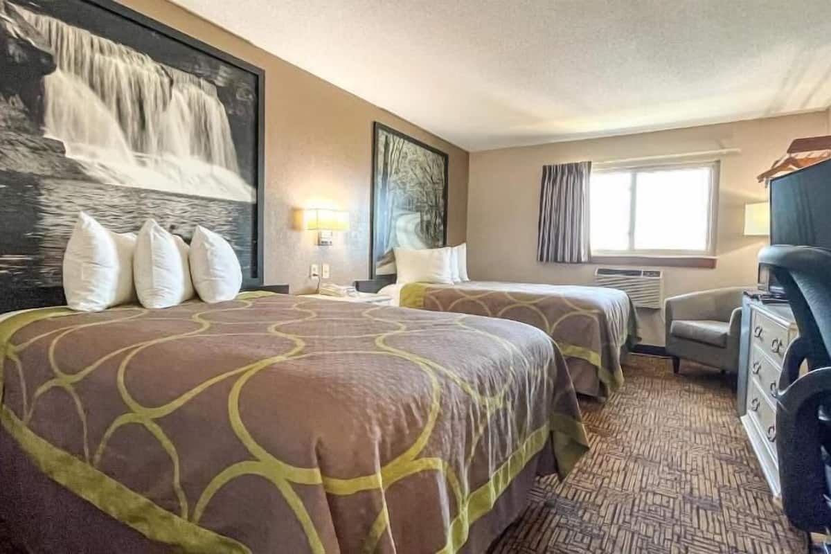 A hotel room with two beds, a desk, a chair, a TV, and artwork on the walls.